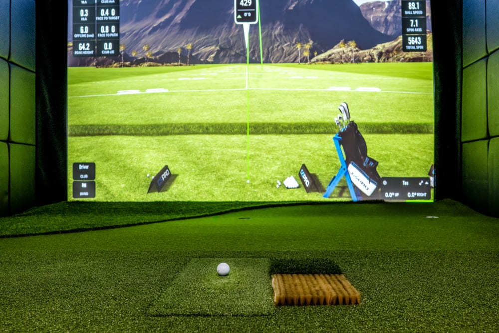 Golf simulator impact screen showing driving range shot data above the hitting mat