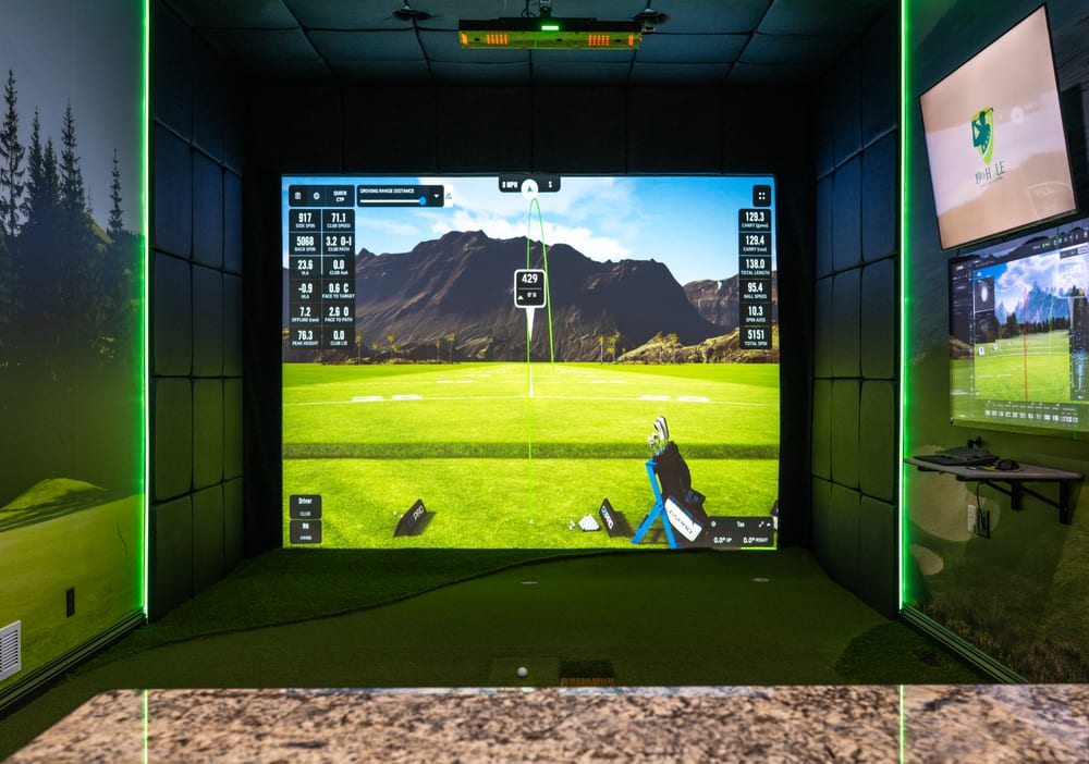 Custom indoor golf simulator bay with padded enclosure, impact screen and side data monitor