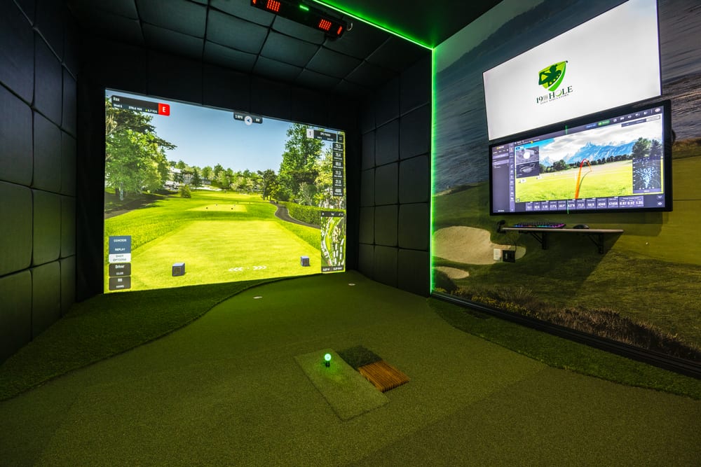 Golf simulator bay laid out in a finished room with turf flooring and hitting mat
